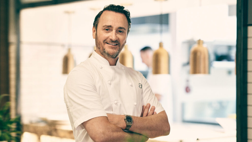 Jason Atherton standing in front of a kitchen with his arms folded