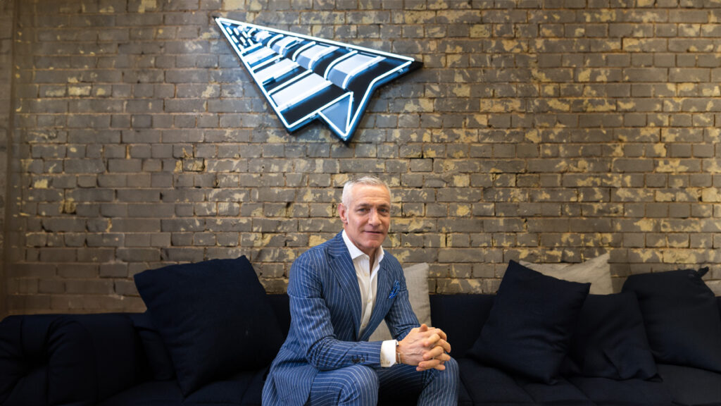 Michael Yormark sitting on sofa with Roc Nation logo above him